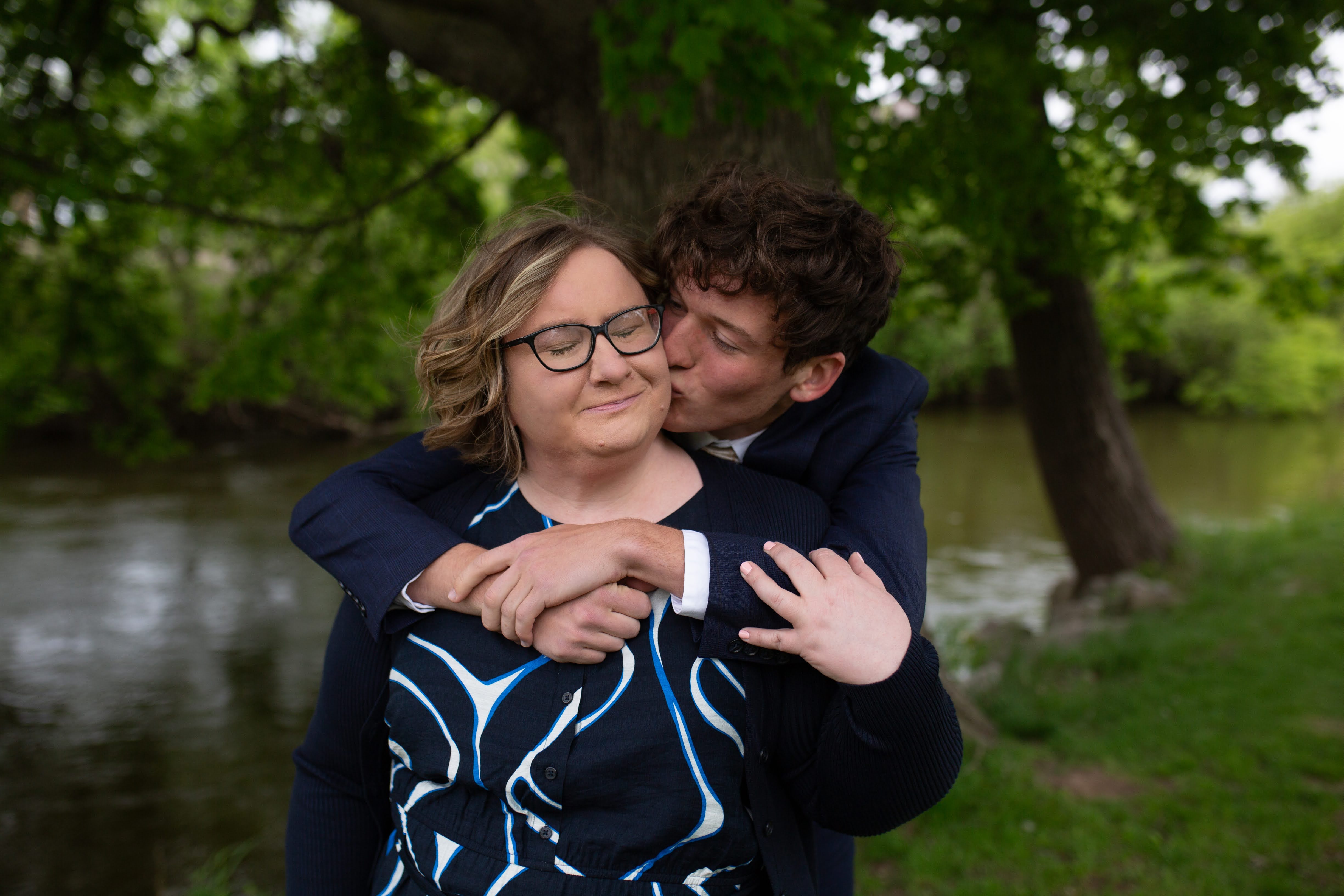 Young man standing behind is mom kissing her cheek.